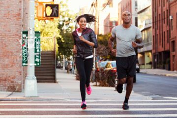 Two people training for a marathon run down the street.